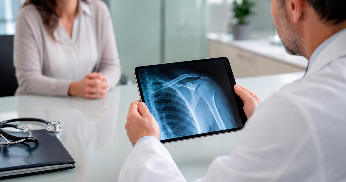 Médico analisa imagem de Raio-X de tórax em tablet diante de paciente